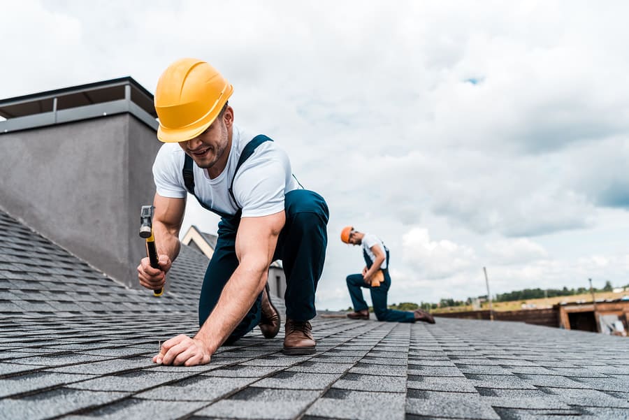 Roofer kneeling on asphalt shingles during a repair